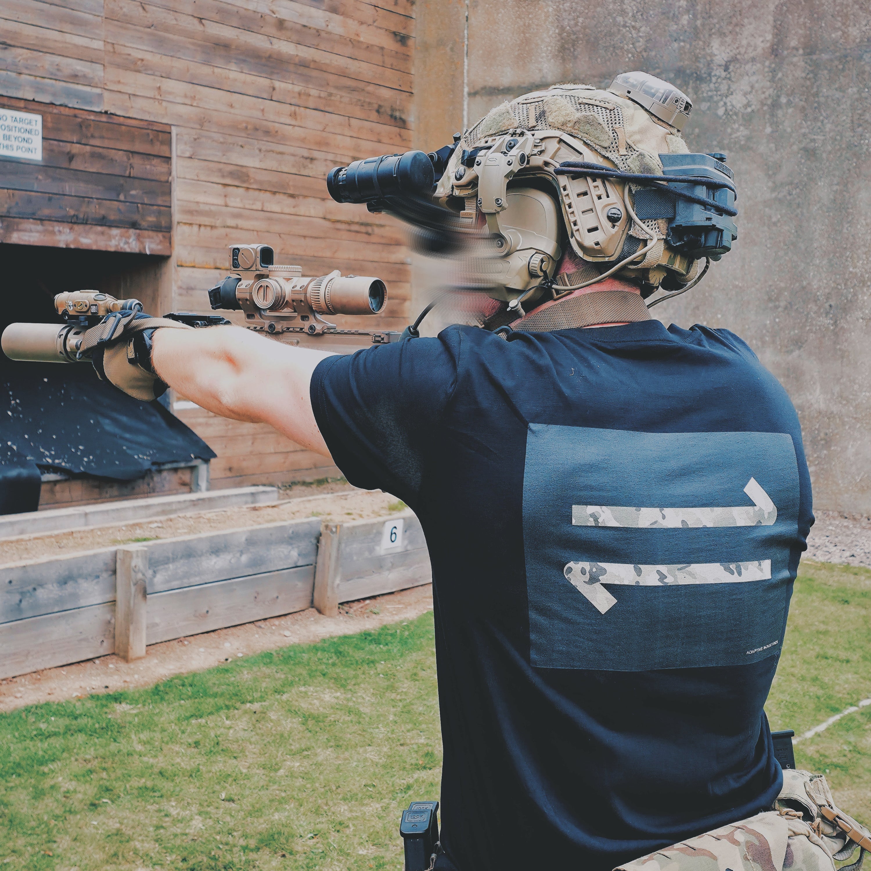 Person in tactical gear aiming a rifle at an outdoor shooting range.
