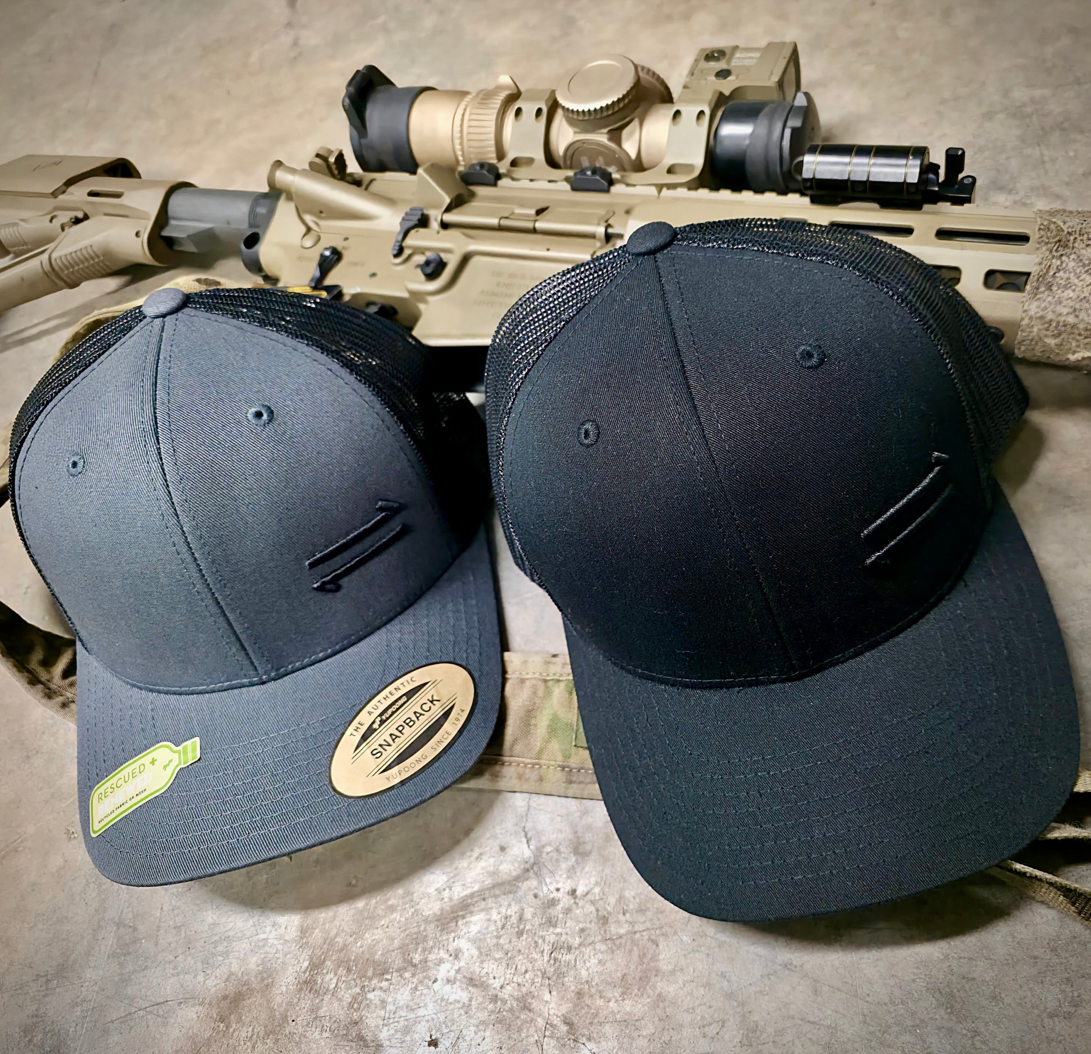 Two tactical hats on a rifle with a concrete background