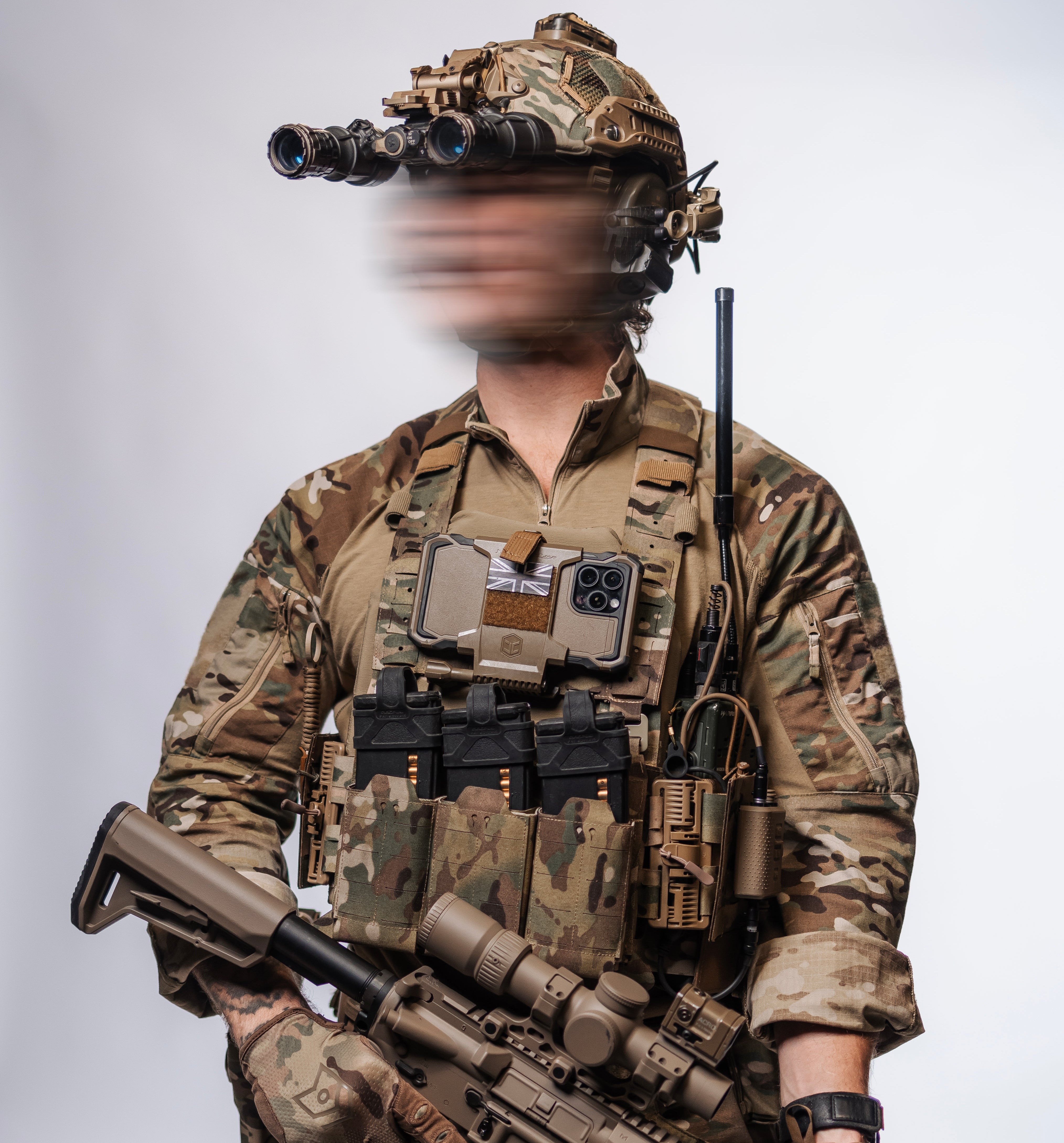 Person in full military gear with camouflage uniform, helmet, and rifle on a plain background