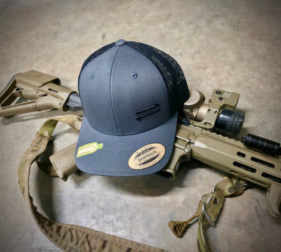 Gray cap with mesh back on a gun and backpack on a concrete floor