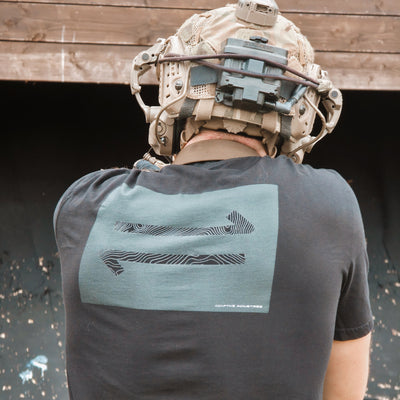 Person wearing a tactical helmet and black t-shirt with a logo, standing against a wooden background.