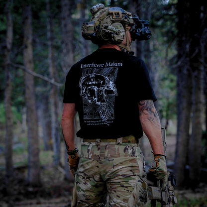 Person in tactical gear with a black t-shirt featuring a skull design in a forest setting