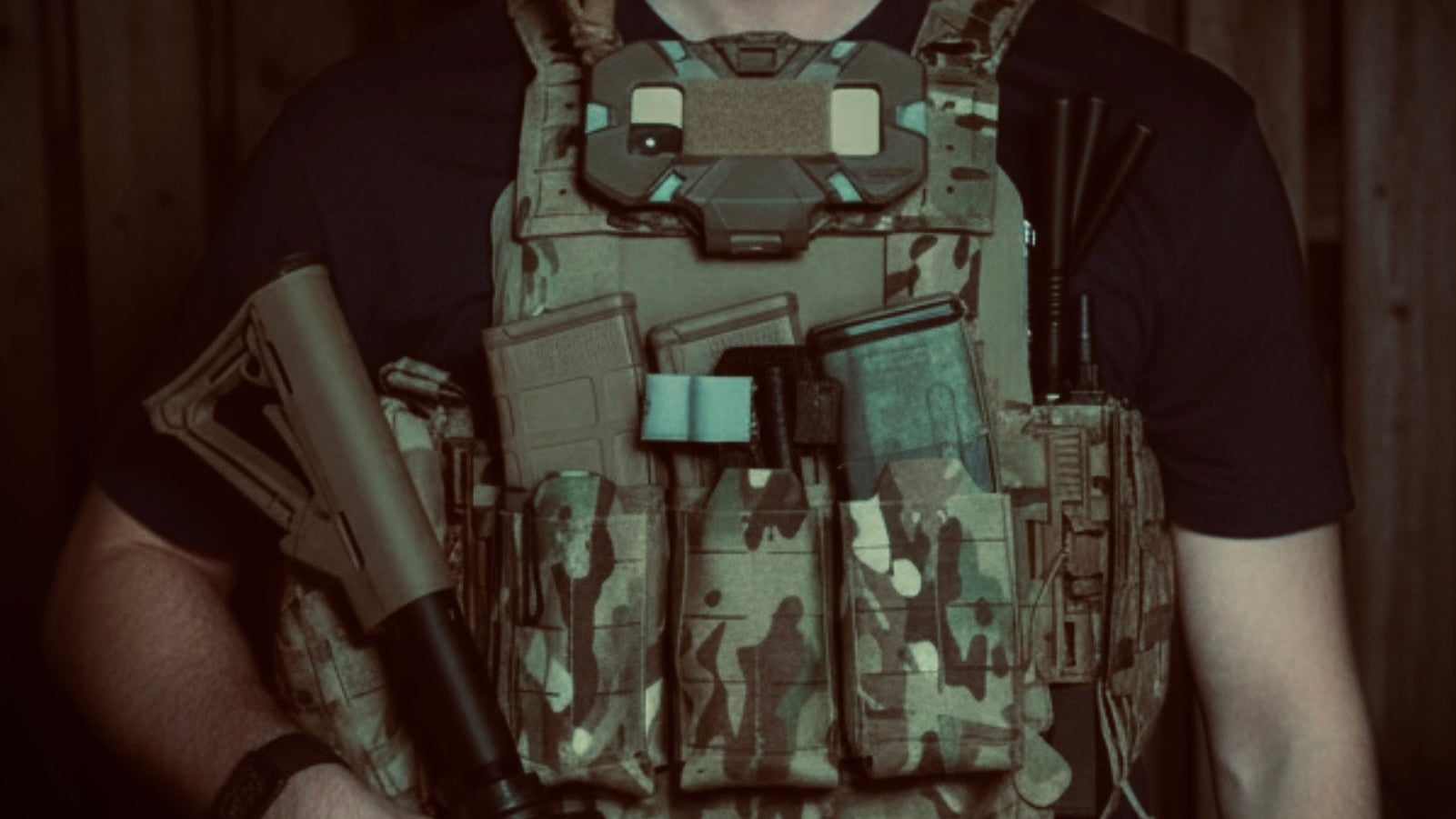 Person wearing a tactical vest and holding a rifle in a dimly lit setting